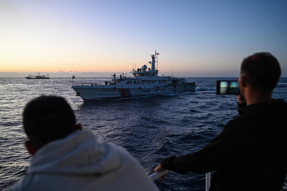 This photo taken on March 5, 2024 shows Philippine Coast Guard personnel filming a China Coast Guard vessel during a supply mission in the disputed South China Sea. Photo by JAM STA ROSA / AFP
