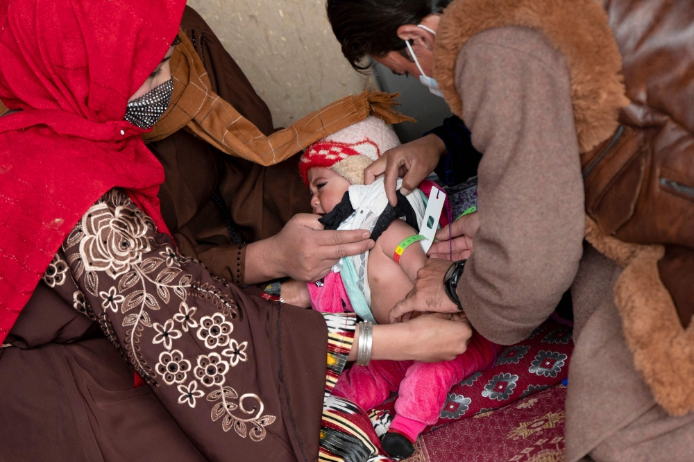 This photograph taken on February 25, 2024 shows Nureddin (R), a member of the Community Health Workers (CHW), examining an Afghan child with a MUAC tape to assess malnutrition at a health post in Gandanchusma village of Badakhshan province. (Photo by Wakil Kohsar / AFP)