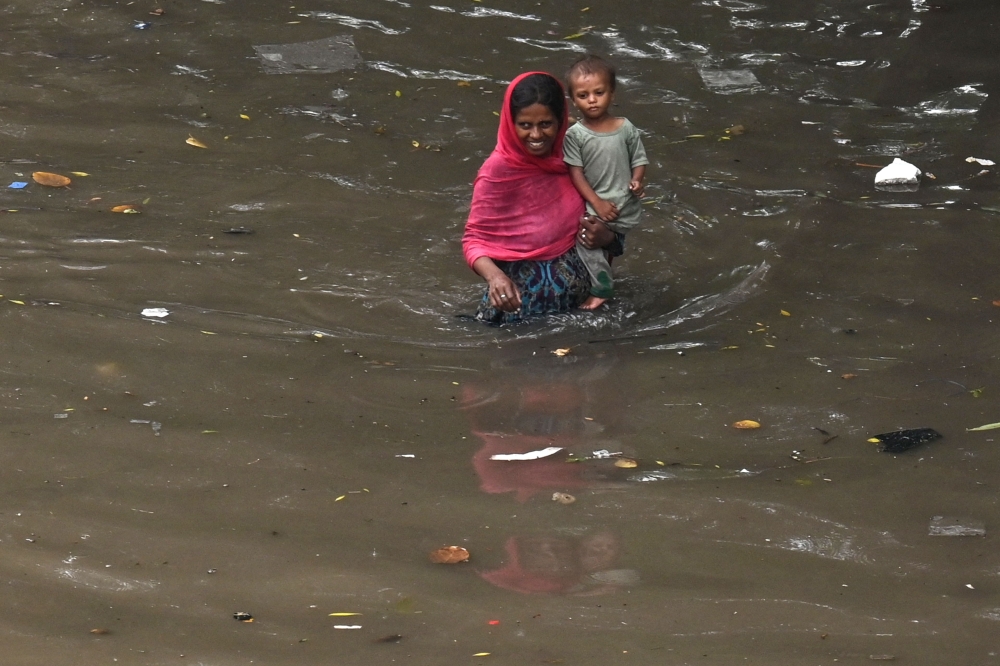 A woman with her child wade through a flooded street amid heavy rainfall in Lahore on August 1, 2024. (Photo by Arif Ali / AFP)