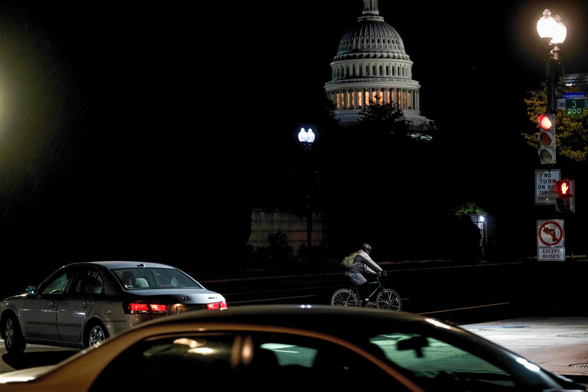 The US Capitol looms in the distance as a man rides his bike up Independence Avenue towards Capitol Hill, on the second day of the US government shutdown in Washington, DC, on October 2, 2025. Photo by Brendan Smialowski / AFP