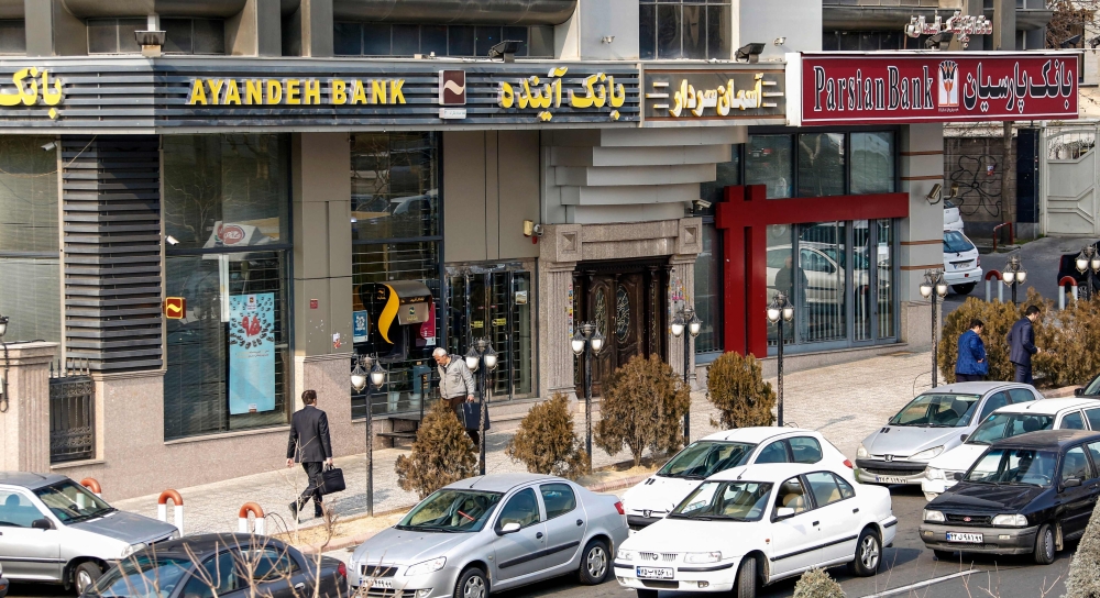 (Files) Iranians walk past an Ayandeh Bank branch (L) in the capital Tehran on January 14, 2017. (Photo by Atta Kenare / AFP)