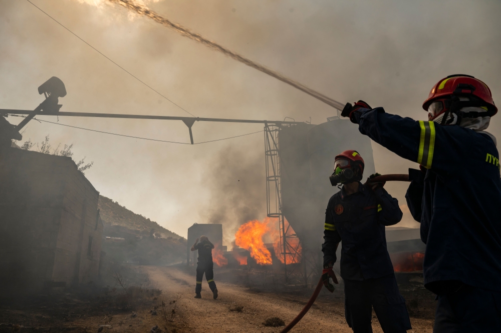 Firemen work to extinguish a fire that broke out at a livestock facility near Kouvaras, south of Athens, on August 10, 2026. (Photo by Aris MESSINIS / AFP)