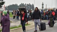 Migrants with their luggage queue to leave the 