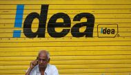 FILE PHOTO: A man speaks on his mobile phone as he sits in front of a shop displaying the Idea Cellular Ltd's logo on its shutter in Mumbai, India, April 28, 2014. Reuters/Danish Siddiqui
