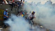 Demonstrators run away from tear gas canisters thrown by the police during a rally against Venezuelan President Nicolas Maduro, in Caracas on April 19, 2017. / AFP.