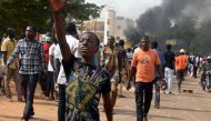 People carry bricks as they walk in front of smoke from a burning tyre during clashes between protesters and police at a demonstration against the 2018 Finance law on October 29, 2017, in Niamey.  AFP / BOUREIMA HAMA
