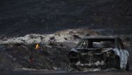 The burnt wreckage of a vehicle is seen along a road as a flames are seen, in the aftermath of the Woolsey fire in Malibu, Southern California, U.S. November 11, 2018. REUTERS/Mario Anzuoni