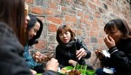 This photograph taken on December 14, 2018 shows Vietnamese women eating 'cha ruoi' ragworms fritters at a street food stall in the old quarters of Hanoi. AFP / Manan Vatsyayana 