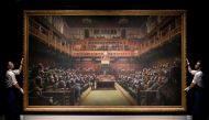 (FILES) In this file photo taken on September 27, 2019 Gallery assistants pose with an artwork entitled 'Devolved Parliament' by British artist Banksy, during a press view in London. AFP / Tolga Akmen