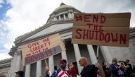 Two men hold signs as they protest against the state's extended stay-at-home order to help slow the spread of the coronavirus disease (COVID-19) as hundreds gather to demonstrate at the Capitol building in Olympia, Washington, U.S. April 19, 2020. REUTERS