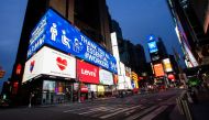 People walk round Times Square as some screens are illuminated in blue as part of the 