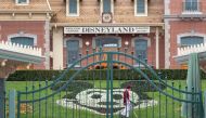 (FILES) In this file photo taken on March 14, 2020 an employee cleans the grounds behind the closed gates of Disneyland Park on the first day of the closure of Disneyland and Disney California Adventure theme parks as fear of the spread of coronavirus con
