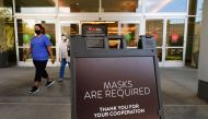 (FILES) In this file photo women wearing facemasks exit a shopping mall where a sign is posted at an entrance reminding people of the mask requirement Westfield Santa Anita shopping mall on June 12, 2020 in Arcadia, California, as Phase 3 in Los Angeles C
