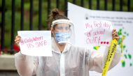 BOSTON, MA - AUGUST 19: A woman in personal protective equipment (PPE) holds up signs at a standout protest organized by the American Federation of Teachers at the Massachusetts State House on August 19, 2020, in Boston, Massachusetts. Scott Eisen/Getty I