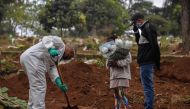 An employee digs next to relatives of a person who died from COVID-19 at the Vila Formosa cemetery, in the outskirts of Sao Paulo, Brazil.  AFP / NELSON ALMEIDA
