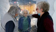 Marie-Paule and Marie-Josephe interact with their mother Colette, 97 old, behind a removable plastic sheet inside a bubble structure which allows families to give hugs without risk of contamination or transmission of Covid-19. Reuters/Pascal Rossignol