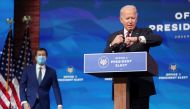 US President-elect Joe Biden looks at his watch as former South Bend, Indiana Mayor Pete Buttigieg arrives behind him to be annouced as his nominee for secretary of transportation during a news conference at Biden's transition headquarters in Wilmington, 