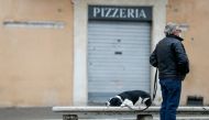 A man stands next to his dog with a closed pizzeria in the background, as the region enters the 'yellow zone' after the government relaxed some of the coronavirus disease (COVID-19) curbs on weekdays following a strict lockdown over the holidays, at Piazz