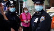 A woman wearing a protective face mask walks by NYPD police officers in the Flushing area of the Queens borough of New York, U.S. March 26, 2021. REUTERS/Shannon Stapleton
