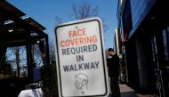 A sign requiring the wearing of a protective face mask is seen as a waiter stands outside a restaurant in Manhasset, New York, U.S. March 29, 2021. REUTERS/Shannon Stapleton
