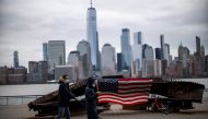 People wear face mask as they walk near a 9-11 memorial during the coronavirus disease (COVID-19) pandemic, while the One World Trade Center and New York skyline are seen from Exchange Place, in New Jersey, U.S., April 2, 2021. REUTERS/Eduardo Munoz
