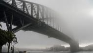 A man wearing a protective face mask takes in the waterfront view underneath the Sydney Harbour Bridge, seen shrouded in fog, during a lockdown to curb the spread of a coronavirus disease (COVID-19) outbreak in Sydney, Australia, June 30, 2021. REUTERS/Lo
