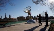 People stand next to a statue featuring the Olympic Rings outside the headquarters of the Beijing Organising Committee for the 2022 Olympic and Paralympic Winter Games in Shougang Park, the site of a a former steel mill, in Beijing, China, November 30, 2021. REUTERS/Thomas Peter/File Photo