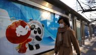 A woman walks past a board with an image of the Beijing 2022 Winter Olympics mascots at a bus stop in Beijing, China January 18, 2022. REUTERS/Tingshu Wang
