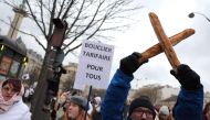 A hold up two crossed baguettes during a protest organised by the collective for the survival of bakers and crafts artisans against the rising energy costs, as they march from from Place de la Nation to Bercy, in Paris on January 23, 2023. (Photo by Thomas SAMSON / AFP)
 