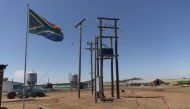A South African flag waves next to electricity poles at the Frangipani Boerdery farm near Lichtenburg on January 23, 2023. - Due to electricity disruptions an estimated of at least 40 000 of broilers died of suffocation on January 16, when insufficient voltage resulted in the air conditioning at one of the farm's chicken houses to shut down. (Photo by GUILLEM SARTORIO / AFP)
