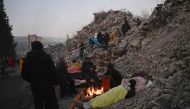 Relatives warm up around a fire in front of rubble of collapsed buildings as rescue teams continue to search victims and survivors, after a 7.8 magnitude earthquake struck the border region of Turkey and Syria earlier in the week, in Kahramanmaras on February 12, 2023. (Photo by Ozan Kose / AFP)