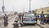 A woman walks past Nigerian police officers at a roadblock at Mile12 Market in Lagos on February 17, 2023, where violence flared up earlier in the day. - Protesters attacked bank ATMs and blocked roads in various Nigerian cities as anger spilled on the streets over a scarcity of cash. (Photo by Michele Spatari / AFP)