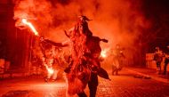 A costumed reveller lights a flare during a procession marking a traditional carnival celebration in the city of Amfissa, central Greece, on February 25, 2023. (Photo by Louisa Gouliamaki / AFP)