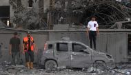 A rescuer and people stand near a burnt car following an Israeli strike in Rafah in the southern Gaza Strip, on October 15, 2023. (Photo by Said Khatib / AFP)