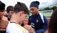 France's forward Kylian Mbappe (R) signs an autograph for a fan wearing a Real Madrid jersey, ahead of a training session, as part of the team's preparation for upcoming UEFA Euro 2024 Football Championship, in Clairefontaine-en-Yvelines on May 30, 2024. Photo by FRANCK FIFE / AFP.