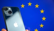 (Files) This photograph shows a hand-held smartphone with the Apple company logo and the European Union logo in the background, in Brussels on September 9, 2024. (Photo by Nicolas TUCAT / AFP)