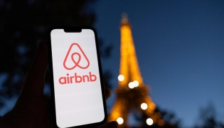 This photograph taken on October 28, 2024 shows the logo of short-term housing rentals online application Airbnb on a smart-phone screen in front of the Eiffel Tower in Paris. Photo by Grégoire CAMPIONE / AFP