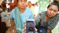 A woman shows a picture of a missing monk during search and rescue operations at a damaged temple in Mandalay on March 30, 2025. (Photo by Sai Aung Main / AFP)