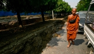 A monk walks past vehicles on the edge of a large crack in the ground along Myo Patt Road linking Mandalay and Sagaing Township on the outskirts of Mandalay on April 2, 2025, five days after a major earthquake struck central Myanmar. Photo by Sai Aung MAIN / AFP