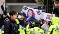 Police stand in front of pro-Yoon supporters on the side of a road as they wait for the arrival of former South Korean president Yoon Suk Yeol (pictured on flag) outside the Central District Court in Seoul on April 14, 2025. Photo by ANTHONY WALLACE / AFP