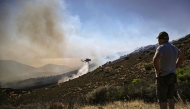 A resident watches a Sikorsky S-64 Skycrane dropping water on a forest fire, near Thymari, southeast of Athens, on June 26, 2025. Photo by Aris MESSINIS / AFP