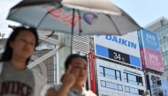 Pedestrians use an umbrella to shelter from the sun as they walk past a digital display (behind) showing a late morning temperature at 34 Centigrade (93.2 F) in the Ginza area of central Tokyo on July 1, 2025. (Photo by Richard A. Brooks / AFP)