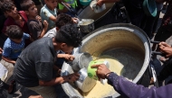 Displaced Palestinians try to take what remains in a pot of lentil soup at a food distribution point in Gaza City in the northern Gaza Strip on July 25, 2025. (Photo by Omar AL-QATTAA / AFP)
