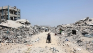 A Palestinian boy pulls a wheelchair past destroyed buildings in the al-Tuffah neighbourhood of Gaza City on August 14, 2025. (Photo by Omar Al-Qattaa / AFP)
