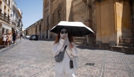 A tourist protects from the sun with a mask and an umbrella during a heatwave in Cordoba, in southern Andalusia region, in Spain, on August 3, 2025. (Photo by Jorge Gurrrero / AFP)