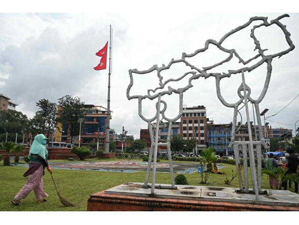 A civic worker walks past Nepal's national flag flying at half-mast next to a structure built in the shape of country's map, in Kathmandu on September 17, 2025. (Photo by Arun Sankar / AFP)