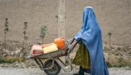 An Afghan burqa-clad woman pushes a wheelbarrow loaded with empty water canisters as she walks along a street in the Koshkak area of the Balkh province on October 5, 2025. (Photo by Atif Aryan / AFP)
