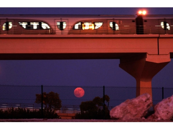 The full moon rises on the horizon as a metro train passes in Doha on October 7, 2025. (Photo by Karim Jaafar / AFP)