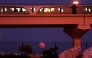 The full moon rises on the horizon as a metro train passes in Doha on October 7, 2025. (Photo by Karim Jaafar / AFP)