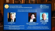 A screen displays the portraits of the 2025 prize winners (L-R) Joel Mokyr, Philippe Aghion and Peter Howitt, during the announcement of the winners of the 2025 Nobel Prize in Economics, the Sveriges Riksbank Prize in Economic Sciences in Memory of Alfred Nobel, at the Royal Swedish Academy of Sciences in Stockholm, Sweden, on October 13, 2025.  (Photo by Jonathan Nackstrand / AFP)